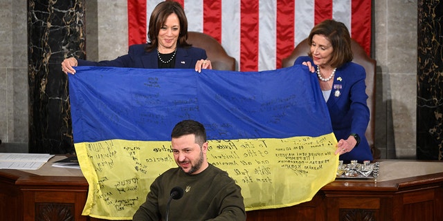 El presidente de Ucrania, Volodymyr Zelensky, se dirige al Congreso de Estados Unidos mientras la vicepresidenta Kamala Harris y la presidenta de la Cámara de Representantes, la demócrata Nancy Pelosi, sostienen una bandera nacional ucraniana que Zelensky les regaló en el Capitolio de Estados Unidos en Washington, DC, el 21 de diciembre de 2022.