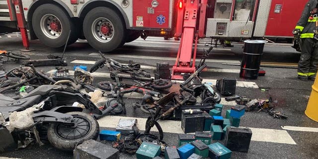 Varias bicicletas eléctricas y baterías de iones de litio esparcidas por la calle mientras los bomberos de Nueva York luchan contra un incendio cercano.